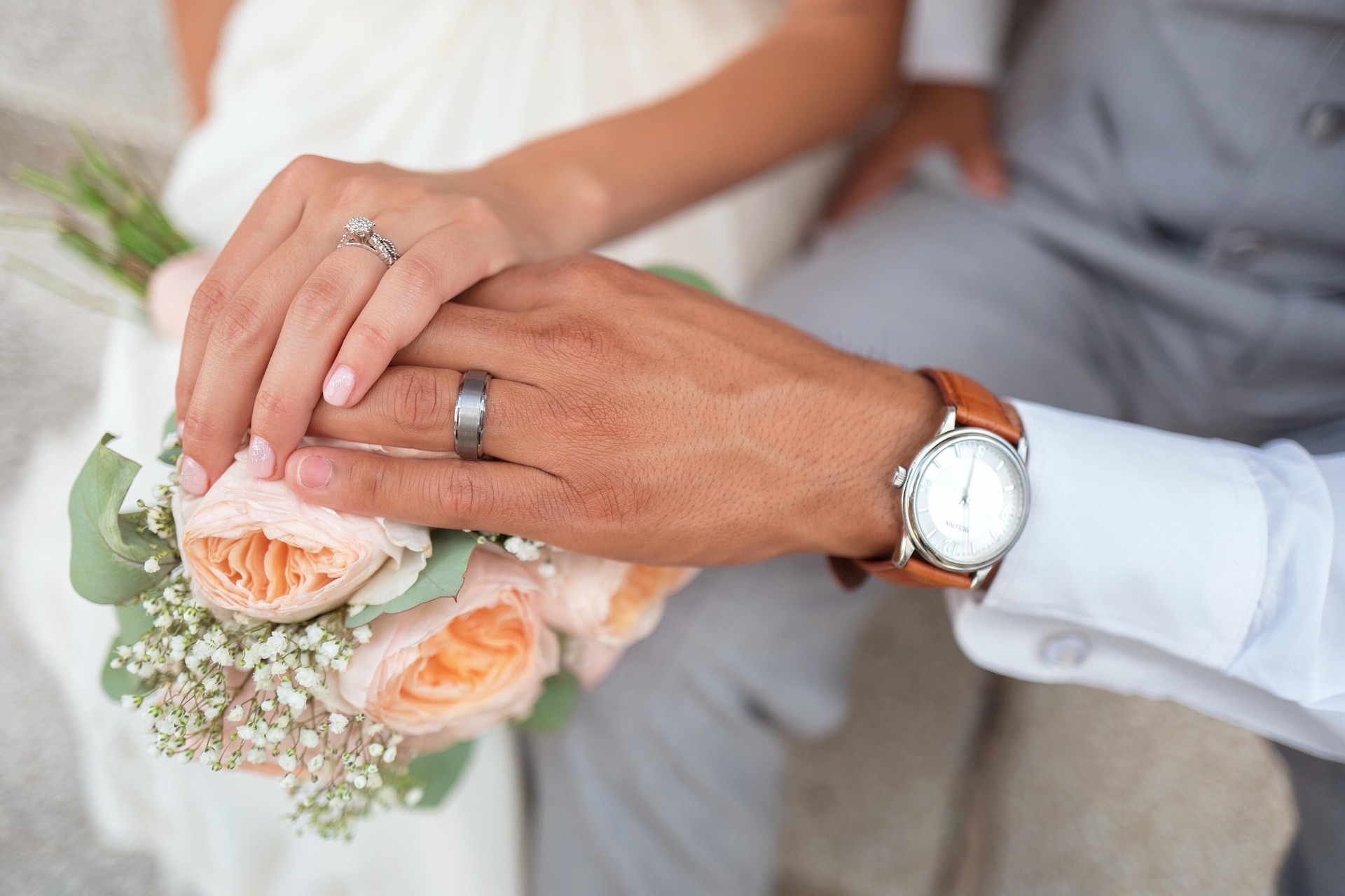 Bride and groom showing wedding rings over a floral bouquet.